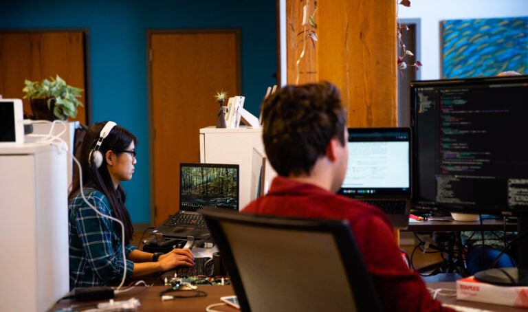 A group of people sitting at their desk looking at computers with software code.