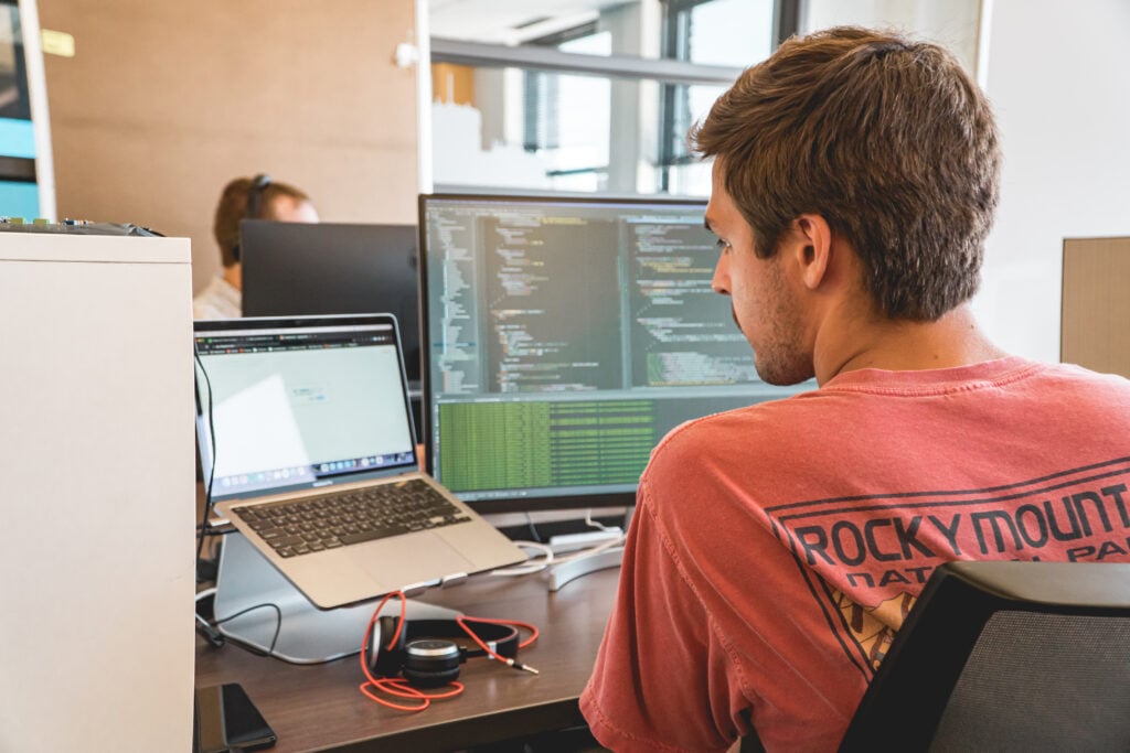 Developer debugging code across multiple monitors at a modern workspace, focused on resolving software issues.